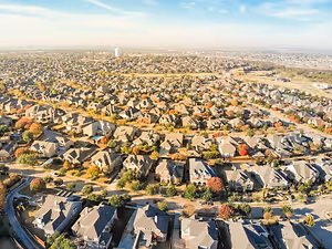 An aerial view of a residential neighborhood with houses, trees, and roads under a blue sky with some clouds.