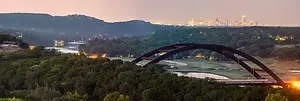 A panoramic view of the city of Austin, Texas, with a bridge and a body of water in the foreground and a city skyline in the background.