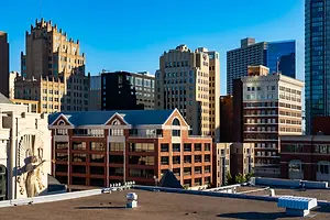 A cityscape with several high-rise buildings, including one with a unique architectural design and a large statue of an angel on its roof.