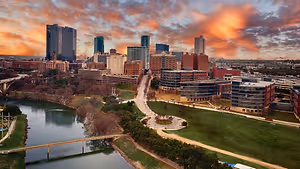 An aerial view of a city with many buildings, a river, and a bridge under a cloudy sky
