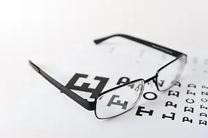 A pair of eyeglasses with prescription lenses placed on top of an eye chart