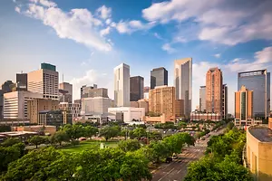 Houston city skyline with tall buildings, green trees, and a blue sky with clouds