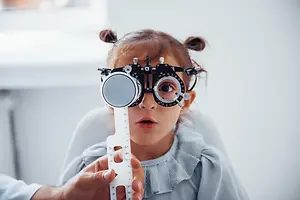 A young girl wearing a black and silver eyeglass with a ruler in her hands and looking at something in front of her