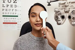 A woman having her eye checked by a doctor with a white eye chart and eye glasses in the background