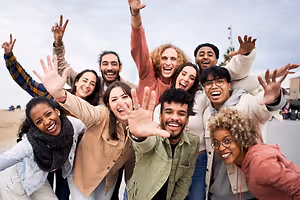 A group of happy people are smiling and waving their hands on the beach, perhaps for a photo