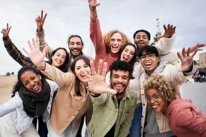 A group of happy people are smiling and waving their hands on the beach, perhaps for a photo