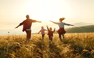 A family of four is running and playing in a golden field at sunset