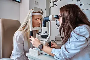 A woman is getting an eye examination in a clinic from a doctor who is holding an ophthalmoscope