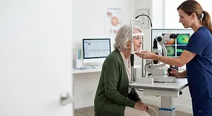 An elderly woman is having her eyes examined by a female optometrist using an eye examination machine in an office setting.