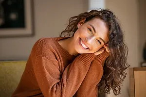 A woman sitting on a couch with her hand on her face and smiling for a photo