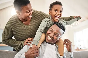 A family of three people, including a man, a woman, and a boy, are smiling while sitting on a couch in a living room.
