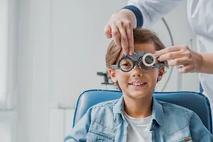 A child is getting their eyes checked by a doctor wearing white coat and holding a metal frame with lenses.