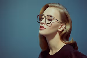 A woman wearing glasses and a black top is looking upwards with her eyes closed