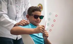 A young boy is getting an eye exam from a doctor who is holding a red tool in front of his face