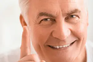 Close up of an older man wearing glasses and adjusting a contact lens.