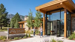 A photo the Littleton eye care center  entrance with people walking in, surrounded by trees and mountains in the background