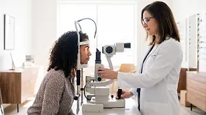 Diverse young woman patient looking into a slit lamp during a contact lens fitting exam in a modern eye clinic