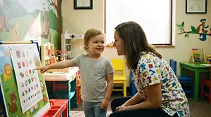 A young child having their vision tested with a colorful pediatric vision chart, optometrist at child's level in a warm clinic