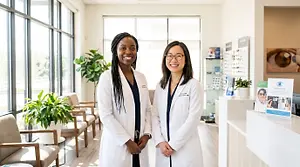 Two female optometrists in white coats in a modern eye care clinic lobby