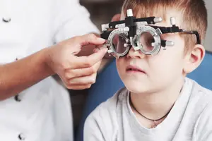 A young boy is having his vision checked by a doctor in a clinic, using specialized equipment.