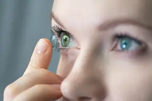 Close up of a woman putting on a colored contact lens in her eye