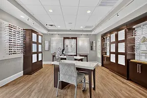 A closeup view of an empty eyeglasses shop with white ceiling lamps and wooden flooring.