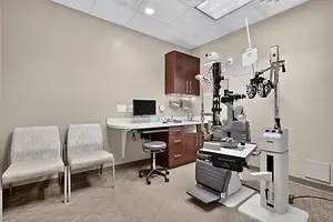 A medical examination room with a desk, chairs, and medical equipment.