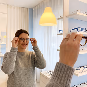 A woman in a gray sweater tries on glasses at an optometrist's office