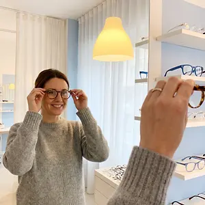 A woman in a gray sweater tries on glasses at an optometrist's office