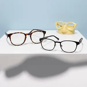 Three pairs of glasses sit on a white surface, including a brown pair, a black pair, and a yellow pair.