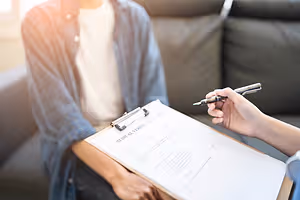 A person is holding a clipboard with a pen and paper while another person is sitting beside them and holding a clipboard with a pen.