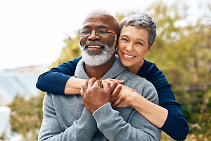 Elderly couple standing outside on a sunny day, smiling and looking at the camera