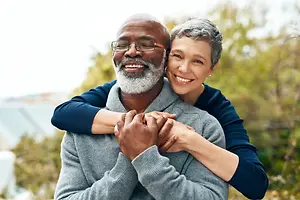 Elderly couple standing outside on a sunny day, smiling and looking at the camera