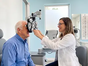 An older man is having his eye examined by an optometrist while sitting in a chair