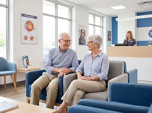 Senior couple talking in an office. The man is wearing glasses and the woman is wearing a watch.