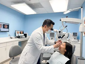 A man in a white lab coat is using a microscope to look into a woman's eye while she sits in a dental chair.