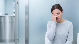 A woman sitting in a chair is holding her head and seems to be feeling unwell.