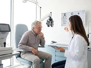 Older man in glasses sitting in an eye doctor's office while the doctor talks to him