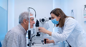 An optometrist using a slit lamp to look into an older man's eye.