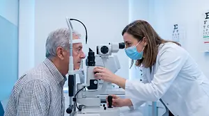 An optometrist using a slit lamp to look into an older man's eye.