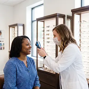 A woman is taking a temperature reading of another woman in an optometrist office.