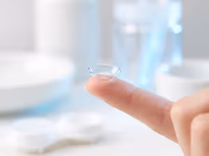 Close-up of a person holding a contact lens with a blurry background