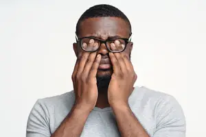 Black man with glasses in studio covering his eyes with his hands