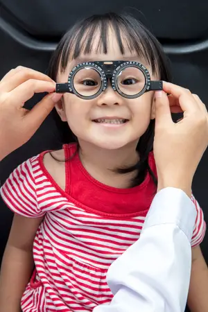 A young girl is having her eyes checked by an eye doctor wearing a white coat.