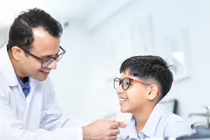 A man wearing glasses and a lab coat examines a boy wearing glasses in a medical setting.