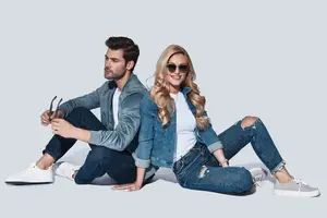 A man and a woman sitting on the floor wearing denim clothing and sunglasses