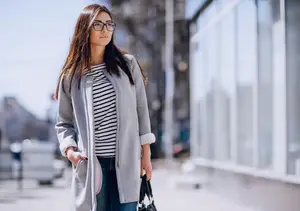 A woman wearing glasses and a jacket is walking on the street, carrying a handbag and looking to the left