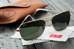 Ray-Ban sunglasses with brown frame and green lenses on a white cloth with a brown leather case in the background.