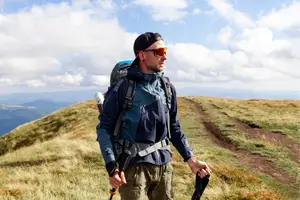 A man hiking with a backpack and trekking poles in a mountainous area with a cloudy sky