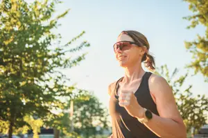 A woman runs in a park with trees and a clear sky in the background.